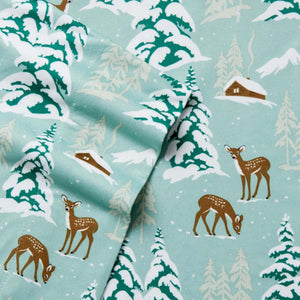 Light blue fabric with a pattern of deer cabins and snow covered pine trees
