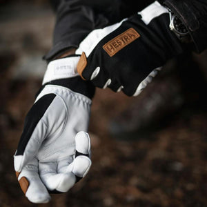 Person wearing black and white Hestra leather gloves with brown logo patch