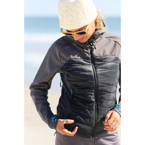 Woman wearing a grey and black hooded jacket with a white beanie and sunglasses on a beach