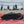 Black geometric portable speaker on a red beach towel with a blurred volleyball net in the background