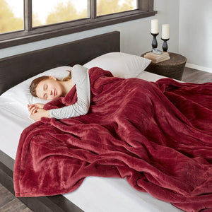 Person sleeping under a red Beautyrest heated throw blanket on a bed