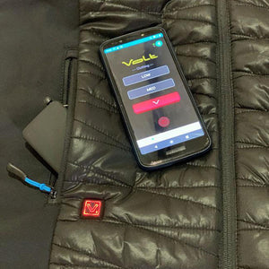 Smartphone displaying Volt Clothing app interface resting on a black quilted heated jacket