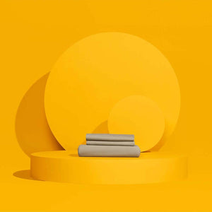 Outlast grey folded bed sheets on a yellow circular pedestal