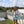 Woman wearing a white denim jacket and light blue dress holding a drink and a mint green cooler bag on a rooftop