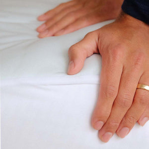 Hands pressing down on a white Outlast mattress protector