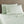 Light green bed sheets and two pillows against a wooden headboard