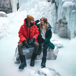 Couple wearing Canada Goose parkas sitting on a rock in a frozen canyon