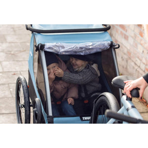 Two children sitting inside a blue Thule bike trailer