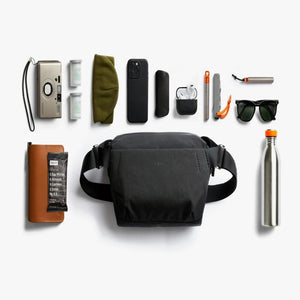Bellroy sling bag surrounded by everyday carry items including a camera phone wallet sunglasses and water bottle