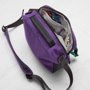 Open purple crossbody bag with internal pockets containing a snack bar and two pencils