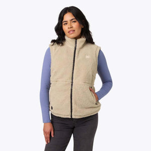 Woman wearing a beige Mobile Warming fleece vest over a blue long sleeve shirt