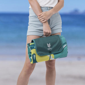 Person holding a folded Cgear sand free beach mat with a green and yellow pattern