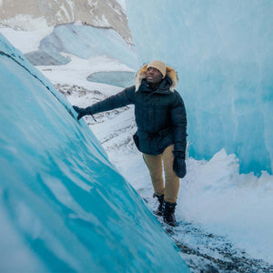 Person in a black parka and tan pants standing between blue glacier walls