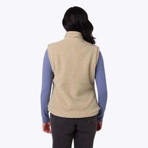 Back view of a woman wearing a beige Mobile Warming sherpa fleece vest over a blue long sleeve shirt