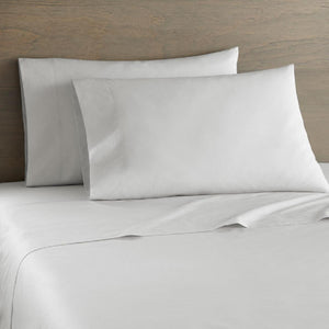White bed sheets and two pillows against a wooden headboard