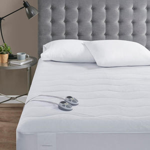 Serta heated mattress pad with two handheld controllers on a bed with a grey tufted headboard