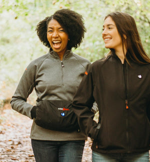 Two women wearing ActionHeat heated jackets and a hand warmer pouch while walking outdoors