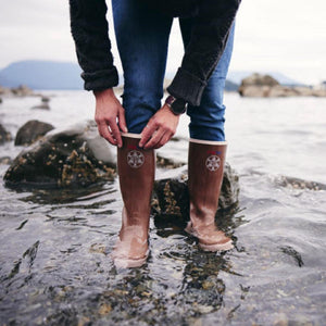 Person wearing brown Xtratuf rubber boots standing in shallow water