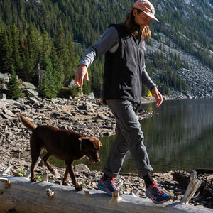 Man wearing a Venture Heat vest walking with a dog on a log by a lake