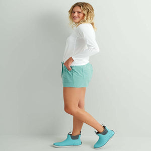Woman wearing a white long sleeve shirt and teal shorts with matching ankle boots