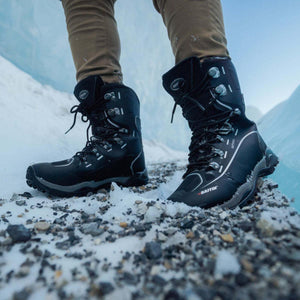 Person wearing black Baffin winter boots on a snowy and rocky surface