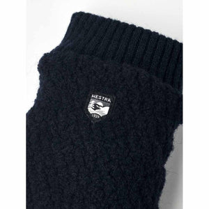 Close up of navy blue Hestra wool mitten with ribbed cuff and brand logo patch