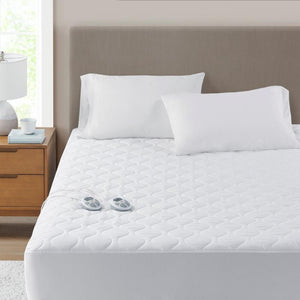 White quilted electric mattress pad with two handheld controllers on a bed with white pillows