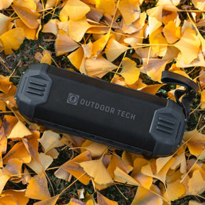 Outdoor Tech portable speaker resting on yellow autumn leaves
