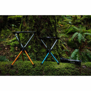 Two Hillsound portable stools with orange and blue legs standing on a mossy log