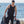 Man wearing a Venture Heat vest and wetsuit holding scuba diving fins and a tank by the ocean