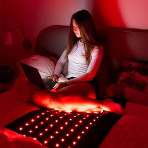 Person using a laptop on a HealthyLine red light therapy mat in bed