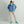 Woman wearing a blue Huk rain jacket and beige pants with a black and white trucker hat
