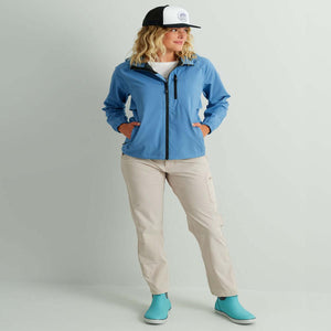Woman wearing a blue Huk rain jacket and beige pants with a black and white trucker hat